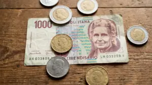 Banconota da 1000 lire con Maria Montessori e monete italiane su un tavolo di legno