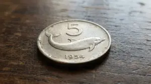 Moneta da 5 lire con delfino del 1954 appoggiata su un tavolo di legno