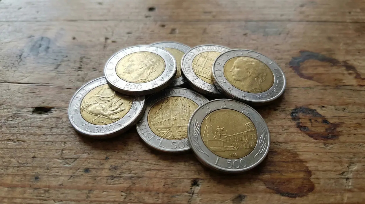 Gruppo di monete italiane da 500 lire bimetalliche appoggiate su un tavolo di legno