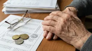 Mani di una persona anziana su documenti con occhiali e monete, simbolo dell’aumento delle pensioni