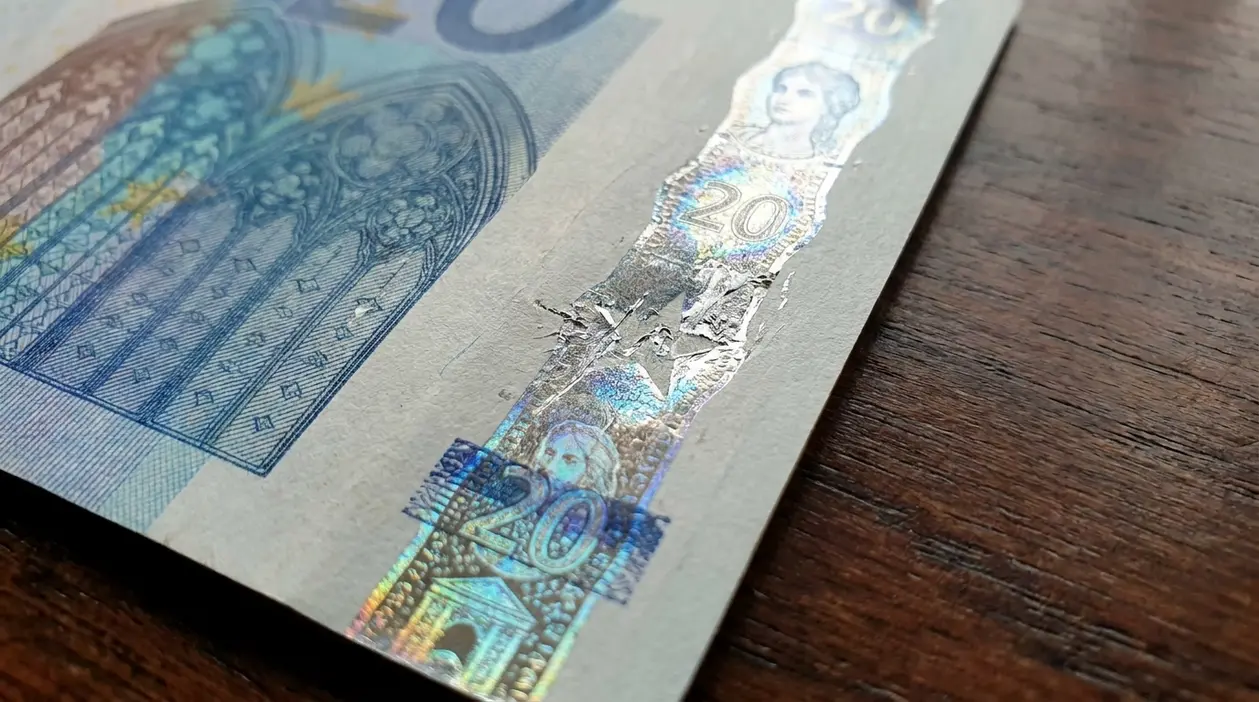 Primo piano di una banconota da 20 euro con banda olografica danneggiata, possibile segno di manomissione