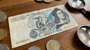Banconota da 500.000 lire italiane su tavolo di legno con monete e lenti d’ingrandimento