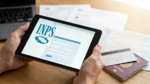 Persona con tablet aperto sul portale INPS per richiedere un bonus, con documenti e carta sul tavolo