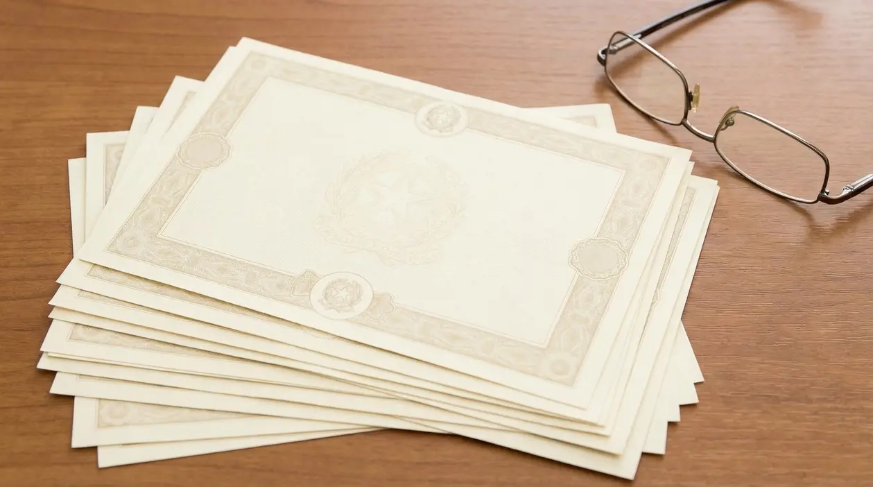 Pile di certificati cartacei su un tavolo di legno con un paio di occhiali, simbolo di investimento sicuro