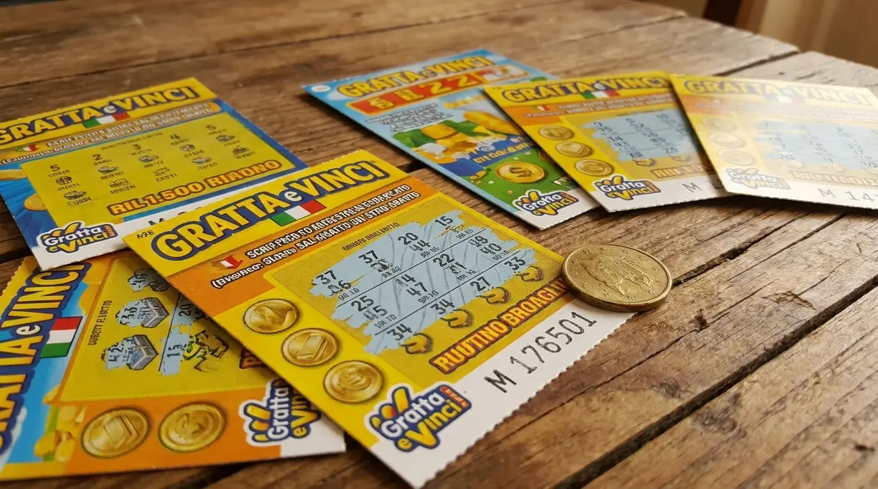 Biglietti Gratta e Vinci sparsi su un tavolo di legno con una moneta accanto