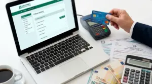Laptop con home banking, carta bancaria, POS, calcolatrice e banconote su una scrivania