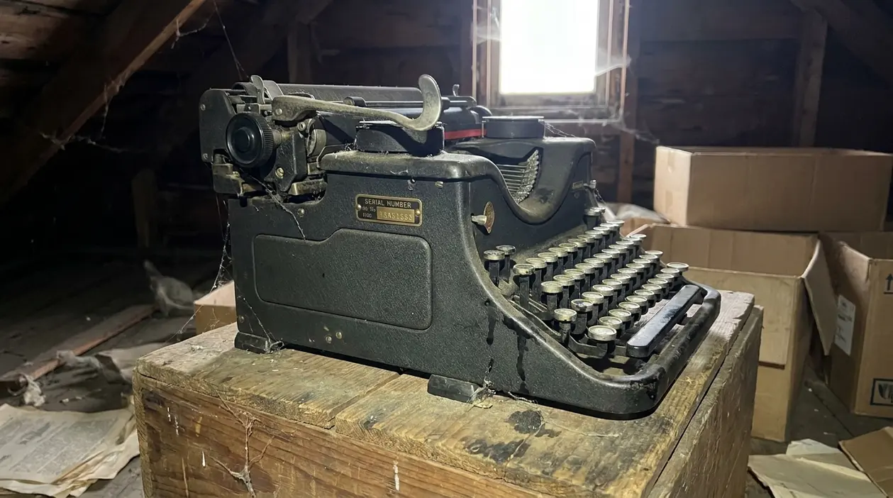 Macchina da scrivere anni ’40 impolverata in soffitta, con targhetta seriale visibile su un tavolo di legno