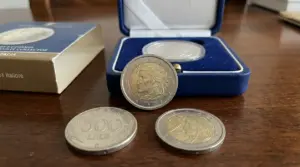 Monete italiane con Dante Alighieri, tra cui 2 euro commemorativi e 500 lire, su un tavolo con cofanetto