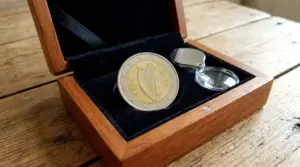 Moneta da 1 euro irlandese con arpa in cofanetto, accanto a una lente d’ingrandimento