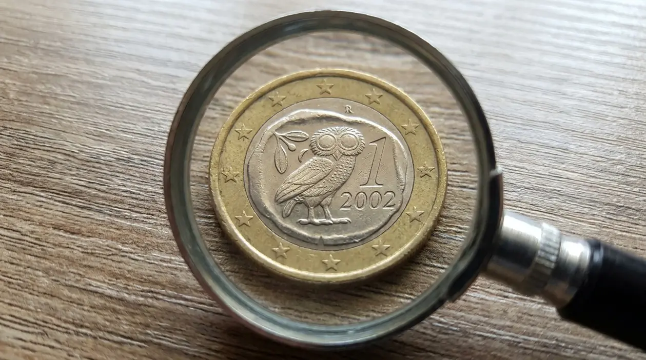 Moneta da 1 euro vista con una lente d’ingrandimento su un tavolo, tema numismatica e valore raro