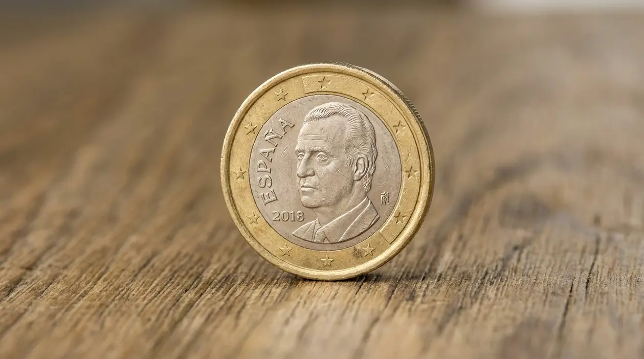Moneta da 1 euro spagnola con volto maschile appoggiata su una superficie di legno