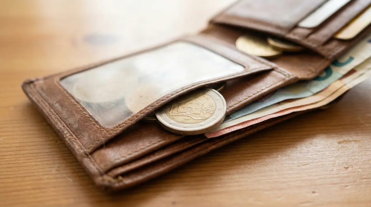 Portafoglio aperto con monete e banconote euro, in evidenza una moneta da 2 euro con una casa