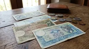 Vecchie banconote da 500 lire e monete italiane su un tavolo di legno accanto a un portafoglio