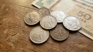 Monete italiane da 50 lire Minerva su un tavolo di legno accanto a una banconota da 50 lire