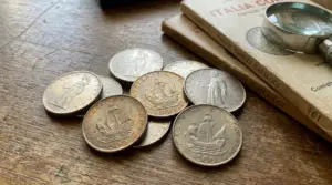 Monete da 500 lire d’argento italiane su un tavolo, accanto a cataloghi numismatici e una lente
