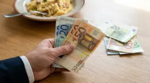 Mano che tiene vecchie banconote da 20 e 50 euro su un tavolo, con altre banconote appoggiate accanto